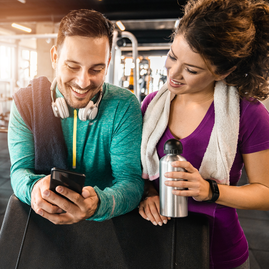 Young man and woman looking at a phone in a gym